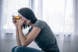 Upset lonely woman with whiskey glass at home
